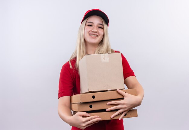 孤立した白い背景の上の歯科ブレース保持ボックスとピザボックスで赤いTシャツとキャップを身に着けている笑顔配達少女