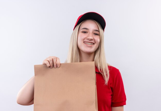 Ragazza sorridente di consegna che indossa la maglietta e il cappuccio rossi in parentesi graffa dentale che tiene tasca della carta su fondo bianco isolato