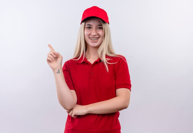 격리 된 흰색 배경에 측면 치과 중괄호 포인트에 빨간 t- 셔츠와 모자를 입고 배달 어린 소녀 미소