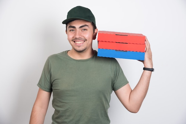 Smiling deliveryman holding three boxes of pizza on white background.