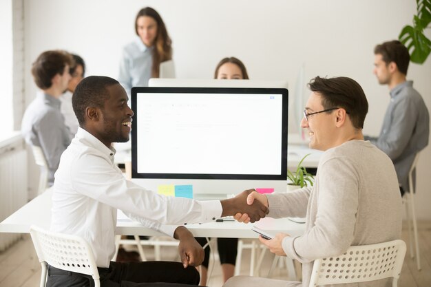 Smiling diverse colleagues handshaking celebrating successful teamwork, thanking for help