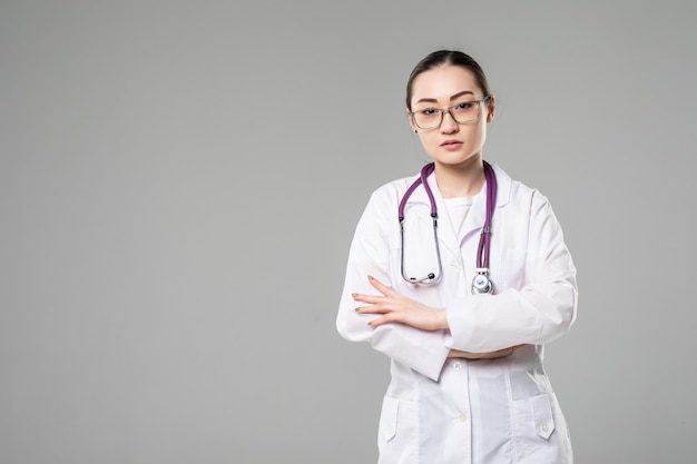 Sorridente medico donna asiatica con le braccia incrociate contro il muro bianco