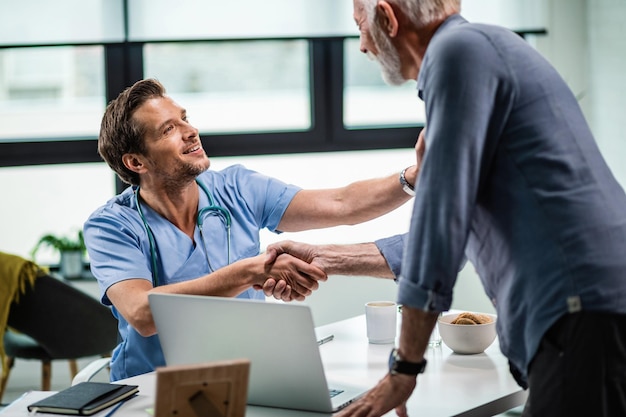 Smiling doctor greeting a mature patient and shaking hands with him at medical clinic