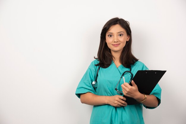 Smiling doctor with stethoscope holding clipboard on white background.