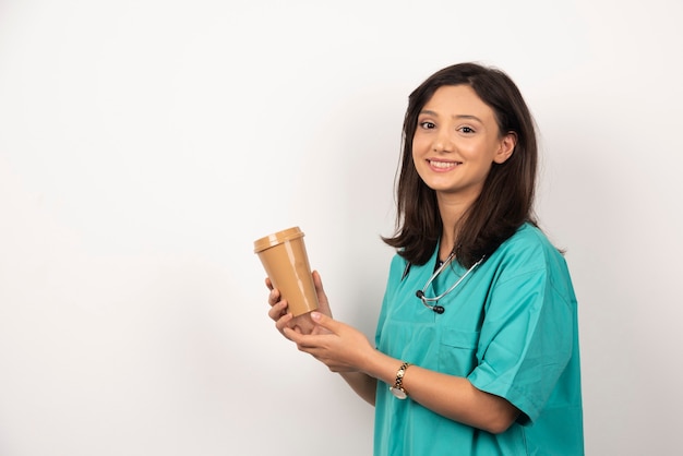 Medico sorridente con lo stetoscopio che tiene tazza su priorità bassa bianca. foto di alta qualità