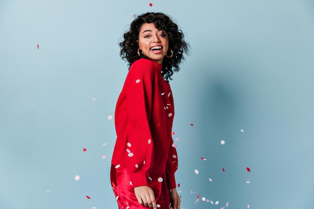 Foto gratuita sorridente ragazza estatica in posa con confetti studio shot di giovane donna di razza mista in maglione rosso casual