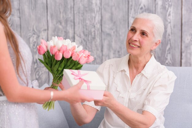 Sorridente donna anziana riceve bouquet di fiori e confezione regalo davanti al suo nipotino