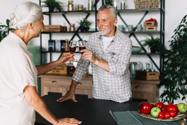 Smiling elderly couple toasting alcohol dinks in the kitchen