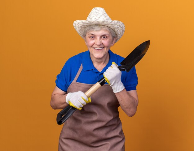 Smiling elderly female gardener wearing gardening hat and gloves holding spade