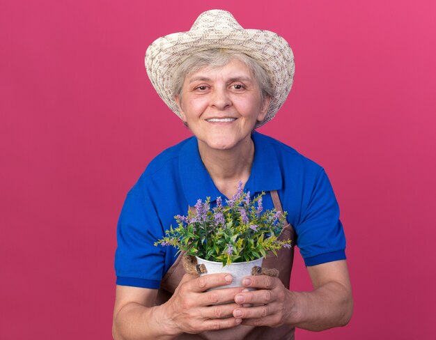 植木鉢を保持しているガーデニング帽子をかぶって笑顔の年配の女性の庭師
