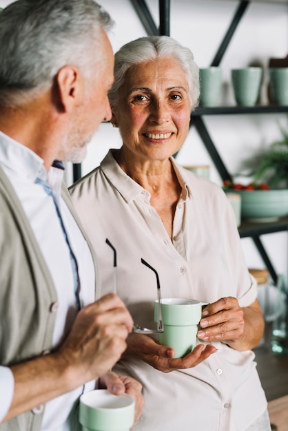 Foto gratuita donna anziana sorridente che tiene tazza di caffè che sta con il suo marito