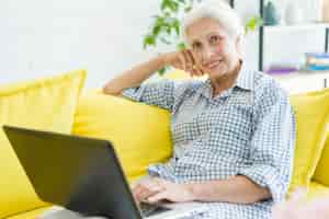 Free photo smiling elderly woman sitting on sofa with laptop