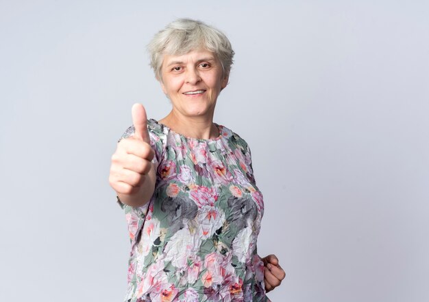 Smiling elderly woman thumbs up isolated on white wall