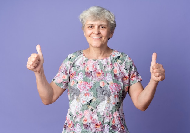 Улыбающаяся пожилая женщина показывает палец вверх двумя руками, изолированными на фиолетовой стене