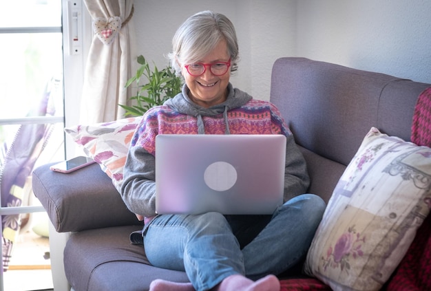 Улыбающаяся пожилая женщина использует ноутбук, делится новостями в блоге и социальных сетях