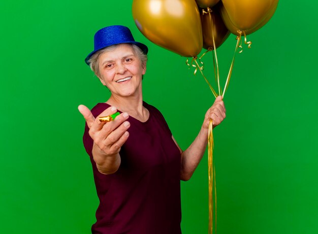 파티 모자를 쓰고 웃는 노인 여성 헬륨 풍선을 보유하고 녹색에 휘파람