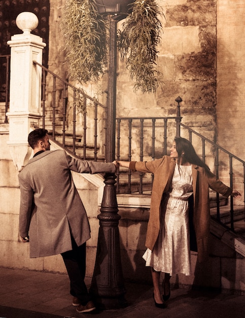 Free photo smiling elegant woman and young man whirling around street lamp