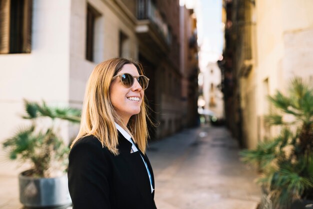 Smiling elegant young woman with sunglasses on narrow street