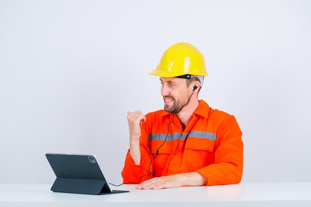 Улыбающийся инженер показывает большим пальцем, сидя перед своим планшетом на белом фоне
