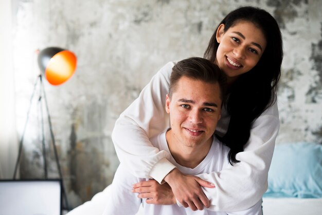 Smiling ethnic woman in white clothes hugging handsome man from behind