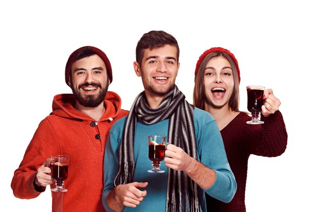 Smiling european men and women during party photoshoot. The guys posing as friends at studio fest with wineglasses with hot mulled wine on foreground.