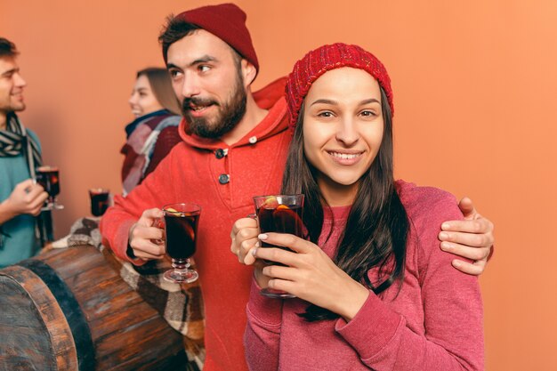 Smiling european men and women during party photoshoot. The guys posing as friends at studio fest with wineglasses with hot mulled wine on foreground.