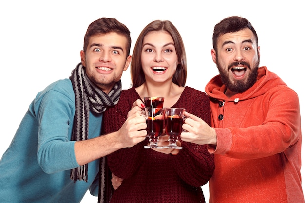 Smiling european men and women during party photoshoot. guys posing as friends at studio fest with wineglasses with hot mulled wine on foreground.