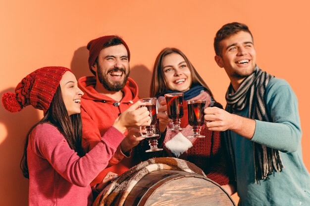 Smiling european men and women during party photoshoot. guys posing as friends at studio fest with wineglasses with hot mulled wine on foreground.