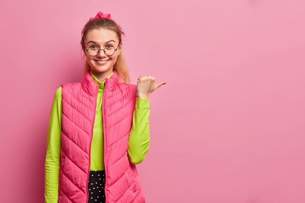 Smiling European woman points away with thumb shows copy space