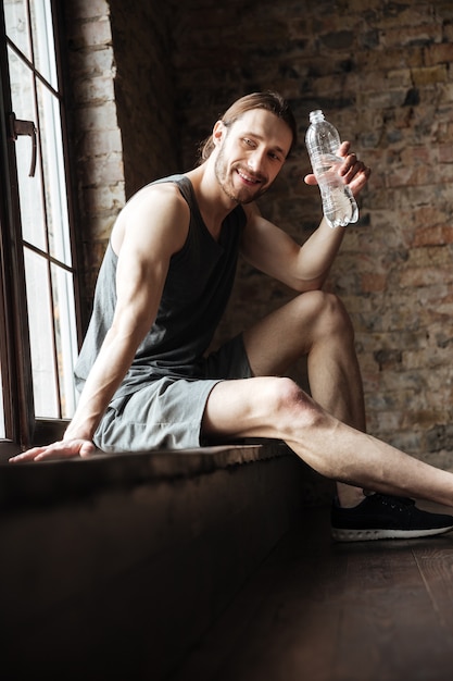 Smiling exhausted sportsman holding water bottle while resting