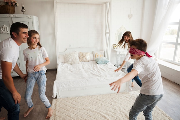 Smiling family playing blind man's buff in bedroom