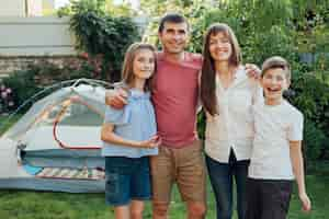 Free photo smiling family standing together in front of tent camp at park