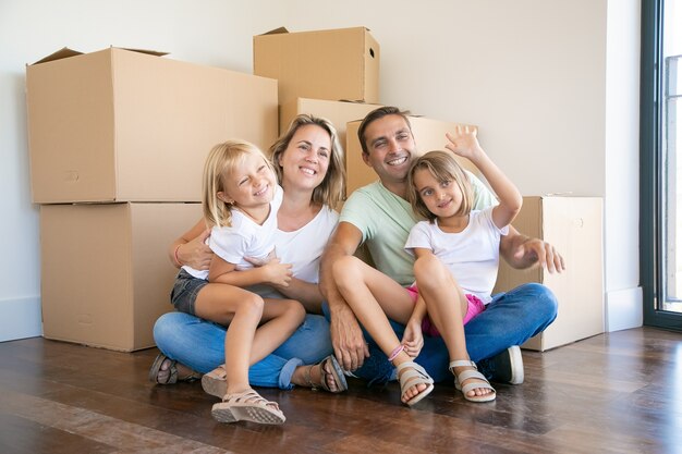 Smiling family with kids sitting on floor near cardboard boxes and relaxing