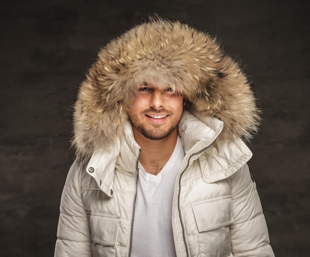 Foto gratuita uomo alla moda sorridente in camice bianco invernale con cappuccio di pelliccia.