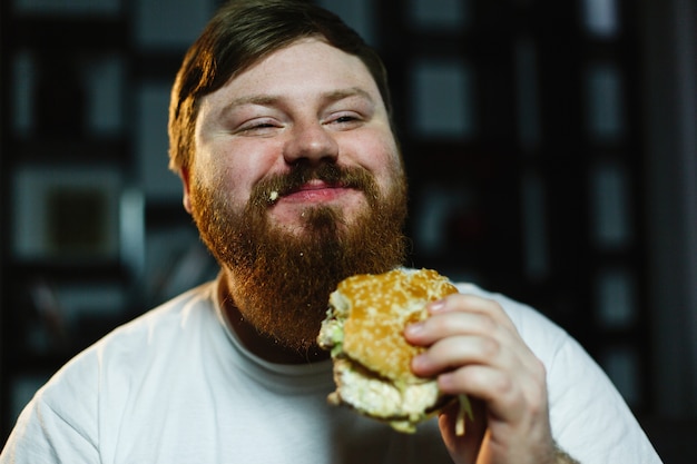 無料写真 笑顔の男は、テレビの前に座っているハンバーガーを食べる