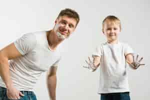 Free photo smiling father and son showing shaving foam on their face and hands on white background