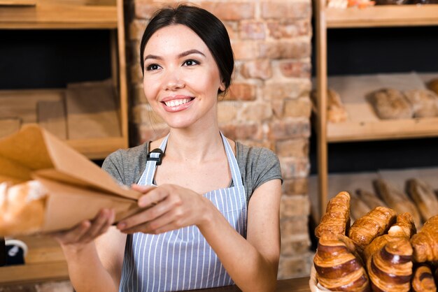 Улыбающаяся женщина-пекарь вручает упакованный хлеб клиенту в пекарне