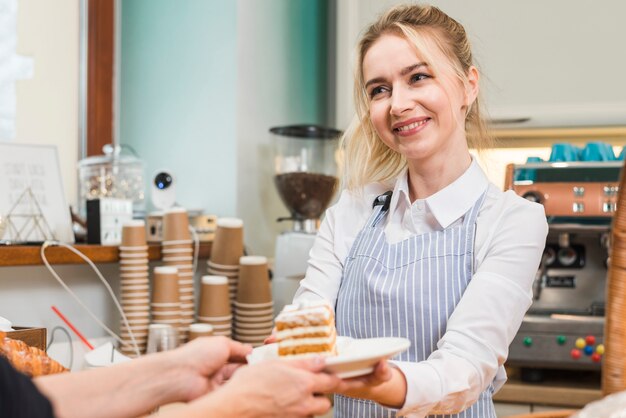 Smiling female baker serving pastry cake to the customer