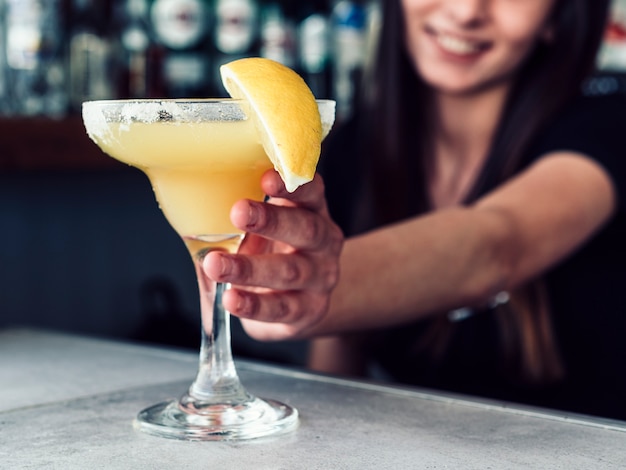 Smiling female bartender serving drink with lemon