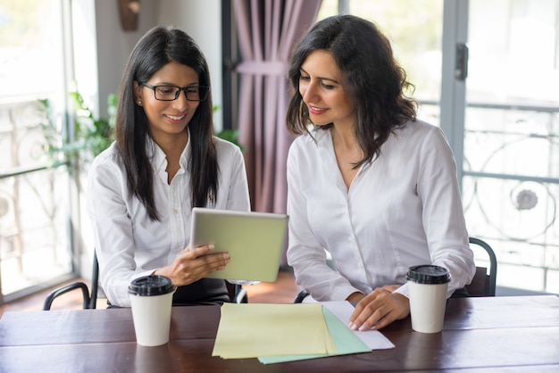 Smiling female business colleagues examining data on touchpad. 