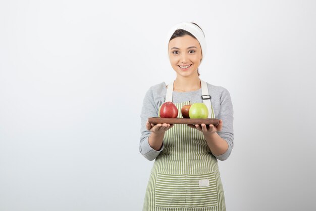 smiling female cook holding plate of apples on white.