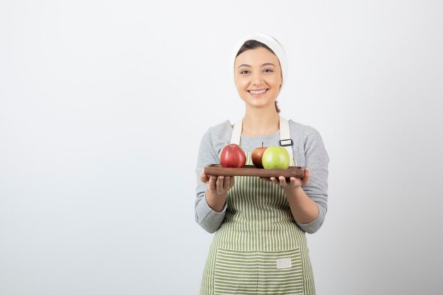 улыбается женщина-повар, держа тарелку яблок на белом.