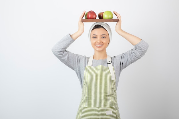 smiling female cook holding plate of apples on white.