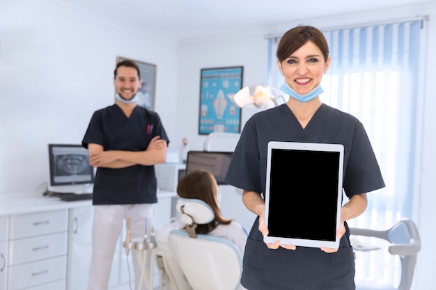 Smiling female dentist showing digital tablet in clinic