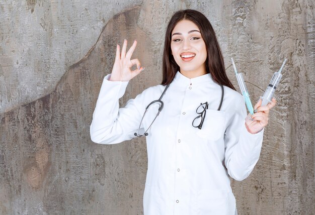 Smiling Female doctor gestures Ok sign and holding syringes