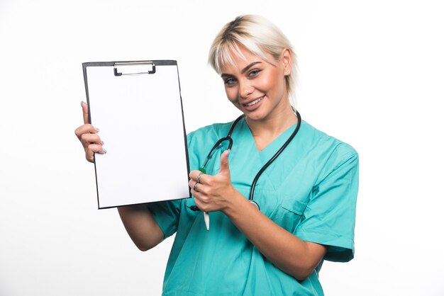 흰색 표면에 엄지 손가락을 보여주는 클립 보드를 들고 웃는 여성 의사
