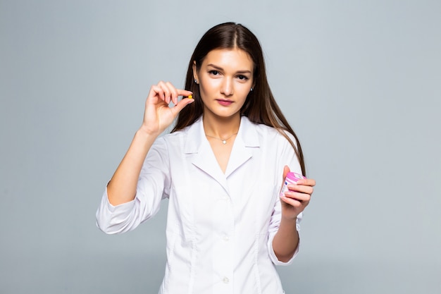 Smiling female doctor holding pills medication isolated on a white wall.