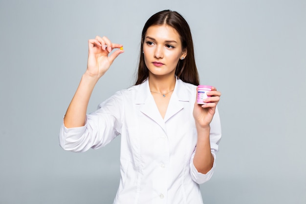 Smiling female doctor holding pills medication isolated on a white wall.