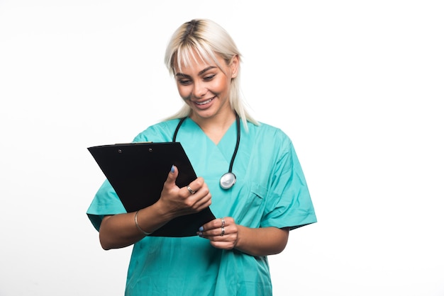 Smiling female doctor looking at a clipboard on white surface