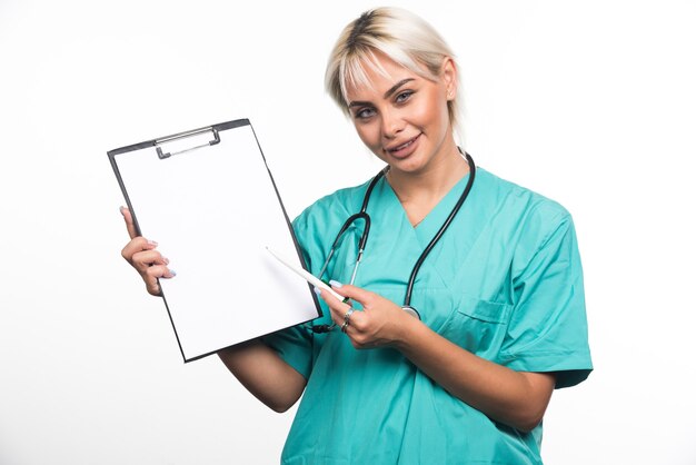 Smiling female doctor pointing a clipboard with pen on white surface